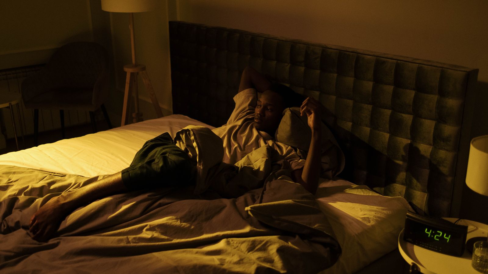 A restless man lying awake in a dimly lit bedroom at night, overthinking and unable to sleep.