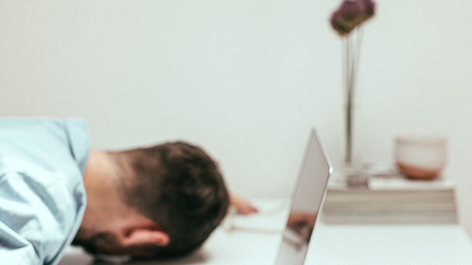 A fatigued man asleep at his office desk with a laptop and coffee mug, illustrating the afternoon energy crash.