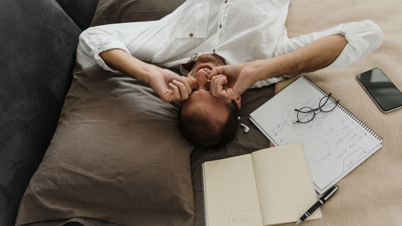 A tired man rubbing his eyes on the couch in the evening, exhausted but unable to relax.